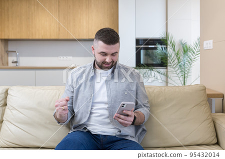 Young man at home sitting on the couch, using the phone, talking on the phone, talking on video 95432014