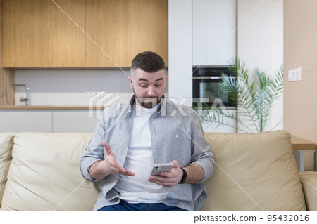 Young man at home sitting on the couch, using the phone, talking on the phone, talking on video 95432016