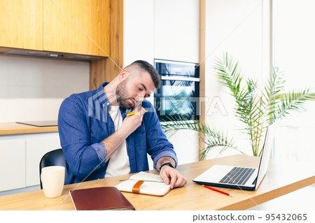 young man at home in the kitchen, working on laptop online, talking on the phone, working with documents, making notes, talking video communication, studying, teaching young man at home in the kitchen, working on laptop online, talking on the phone, working with documents, making notes, talking video communication, studying, teaching 95432065