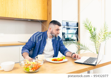 young man at home in the kitchen, cooking online, working on laptop young man at home in the kitchen, cooking online, working on laptop 95432077