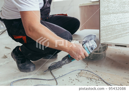 male worker cuts a large ceramic tile with an electric saw with a hand tool 95432086