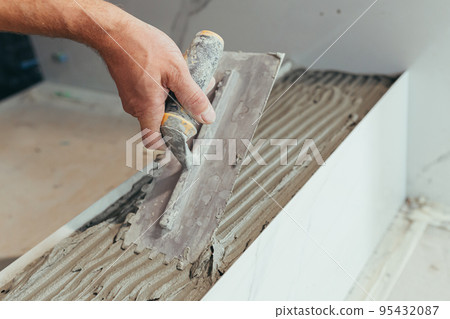 Male worker professional mounts ceramic tile in bathroom photo with close spatula with glue 95432087