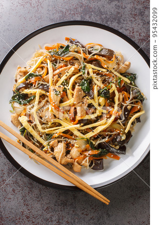 japchae or stir-fried Korean vermicelli noodles with vegetables and pork topped with sesame closeup on the plate. Vertical top view japchae or stir-fried Korean vermicelli noodles with vegetables and pork topped with sesame closeup on the plate. Vertical top view 95432099
