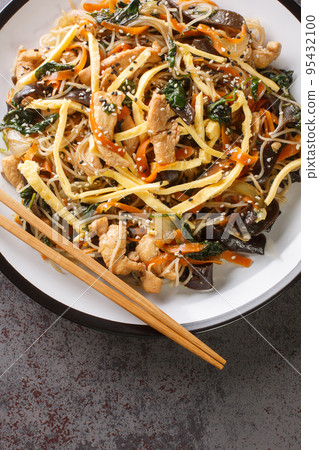 Japchae Korean Glass noodle stir fry with eggs, vegetables and mushrooms closeup on the plate. Vertical top view 95432100
