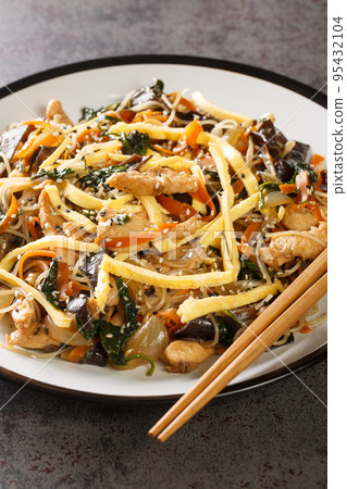 Japchae Korean Glass noodle stir fry with eggs, vegetables and mushrooms closeup on the plate. Vertical 95432104