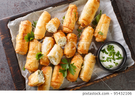 Borek is a Turkish pastry with savory filling with cheese and spinach closeup on the wooden board. Horizontal top view Borek is a Turkish pastry with savory filling with cheese and spinach closeup on the wooden board. Horizontal top view 95432106