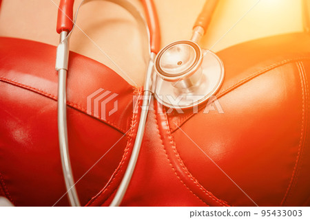 Young woman in red corset and black leather pants with a phonendoscope. Sexy brunette nurse in red and black costume with stethoscope in her hands. Role doctor play. Celebration and party. Having fun 95433003