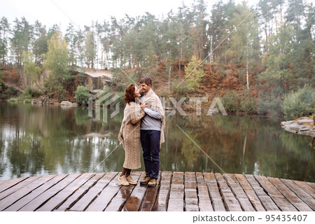 Happy couple travels in autumn in picturesque place among rocks and water. Covered with blanket from rain. Soft focus .Ukraine, Korostyshiv quarry. Happy couple travels in autumn in picturesque place among rocks and water. Covered with blanket from rain. Soft focus .Ukraine, Korostyshiv quarry. 95435407