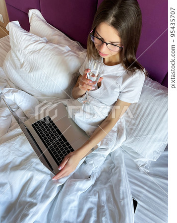 Young woman on the bed typing and working on a laptop 95435707