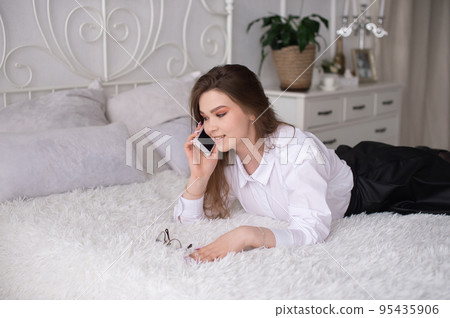 Energetic cute girl is lying on the bed with a phone 95435906