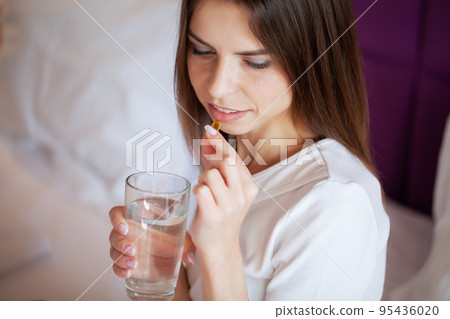 Profile of happy girl taking omega 3 pill on bed in morning at home 95436020