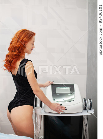 Red-haired woman in a medicine salon, anti-cellulite procedure. Red-haired woman in a medicine salon, anti-cellulite procedure. 95436101