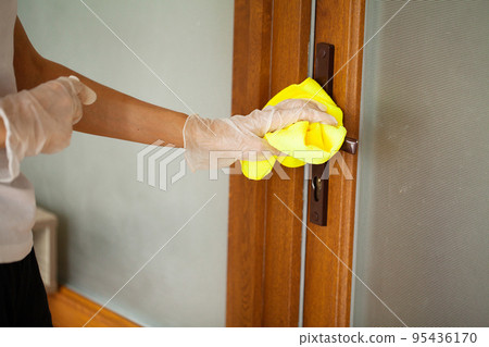 Woman cleaning door, door knob with alcohol spray at the house. Woman cleaning door, door knob with alcohol spray at the house. 95436170
