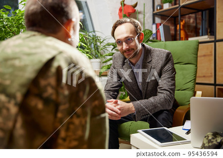 Young distressed woman in military uniform talking to psychologist during therapy session, indoors. Help, support, ptsd, health and harmony concept 95436594