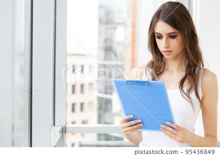A woman in the office near the window, holding documents in her hands 95436849