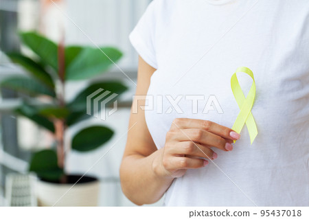 Woman in white t-shirt holding and showing yellow awareness ribbon in her hands Woman in white t-shirt holding and showing yellow awareness ribbon in her hands 95437018