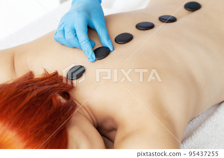 Professional beautician massaging female back by stones in beauty studio Professional beautician massaging female back by stones in beauty studio 95437255