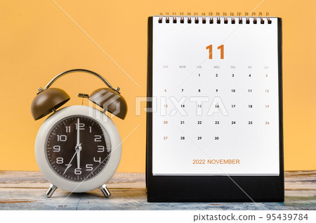 The November 2022 Monthly desk calendar for 2022 year and Alarm clock vintage on wooden table. 95439784