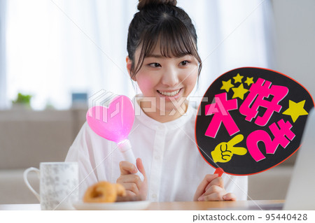 Oshikatsu A young woman who cheers for the Oshi by waving a fan while watching a live video 95440428