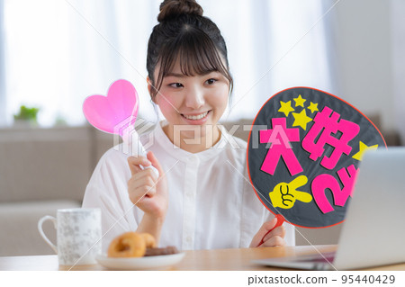 Oshikatsu A young woman who cheers for the Oshi by waving a fan while watching a live video Oshikatsu A young woman who cheers for the Oshi by waving a fan while watching a live video 95440429