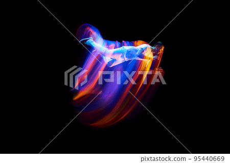 Creative dynamic portrait of athlete, dancer in white sports clothes jumping, flying over dark background in mixed neon light, glow. Art, aspiration, music, fashion 95440669