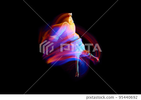 Creative dynamic portrait of athlete, dancer in white sports clothes jumping, flying over dark background in mixed neon light, glow. Art, aspiration, music, fashion 95440692