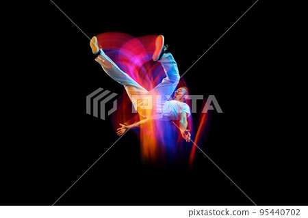 In miracle flight. Young sportive dancer in white clothes levitating, moving over dark background in mixed neon light. Creative art, aspiration, music, fashion, dance 95440702