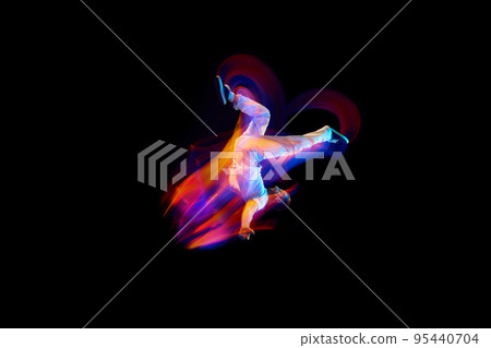 Dance in motion. Studio shot of flying, jumping dancer or gymnast performing tricks in the air over black background with mixed neon glowing rays Dance in motion. Studio shot of flying, jumping dancer or gymnast performing tricks in the air over black background with mixed neon glowing rays 95440704