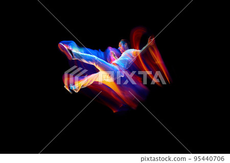 Creative dynamic portrait of athlete, dancer in white sports clothes jumping, flying over dark background in mixed neon light, glow. Art, aspiration, music, fashion 95440706