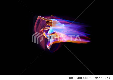 In miracle flight. Young sportive dancer in white clothes levitating, moving over dark background in mixed neon light. Creative art, aspiration, music, fashion, dance In miracle flight. Young sportive dancer in white clothes levitating, moving over dark background in mixed neon light. Creative art, aspiration, music, fashion, dance 95440765