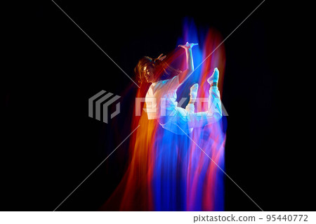 In miracle flight. Young sportive dancer in white clothes levitating, moving over dark background in mixed neon light. Creative art, aspiration, music, fashion, dance 95440772