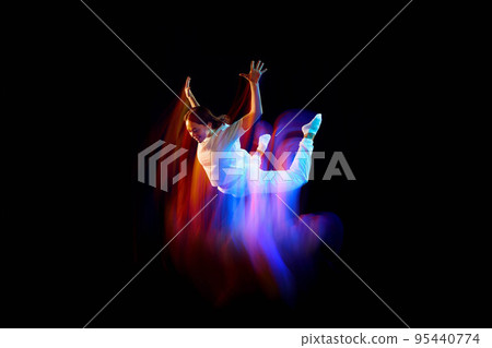 Creative dynamic portrait of athlete, dancer in white sports clothes jumping, flying over dark background in mixed neon light, glow. Art, aspiration, music, fashion 95440774