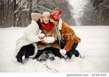 Joyful teens and their beautiful mother spending time together in the winter park. Family riding on a sled. Family wearing warm jackets and knitted hats. Joyful teens and their beautiful mother spending time together in the winter park. Family riding on a sled. Family wearing warm jackets and knitted hats. 95441939
