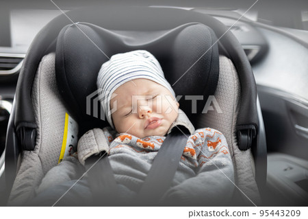 Cute little baby boy sleeping strapped into infant car seat in passenger compartment during car drive. Cute little baby boy sleeping strapped into infant car seat in passenger compartment during car drive. 95443209