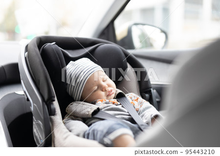 Cute little baby boy sleeping strapped into infant car seat in passenger compartment during car drive. Cute little baby boy sleeping strapped into infant car seat in passenger compartment during car drive. 95443210