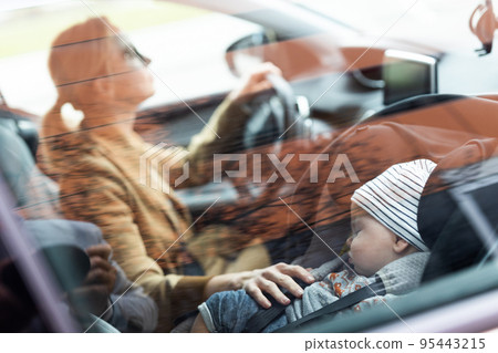 Mother concentrating on driving family car running errands while her baby sleeps in infant car seat by her site. 95443215