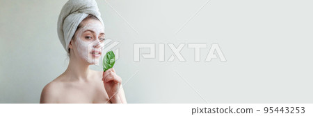 Beauty portrait of woman in towel on head with white nourishing mask or creme on face and green leaf in hand, white background isolated. Skincare cleansing eco organic cosmetic spa concept Beauty portrait of woman in towel on head with white nourishing mask or creme on face and green leaf in hand, white background isolated. Skincare cleansing eco organic cosmetic spa concept 95443253