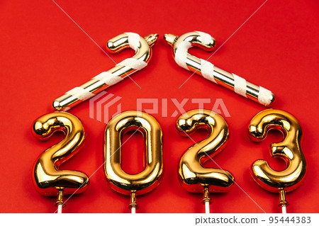 festive red background with gold numbers 2023 and gold decorative candy canes in form of house roof. 95444383