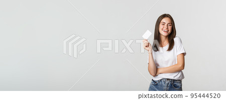 Attractive happy brunette girl laughing and holding credit card, white background Attractive happy brunette girl laughing and holding credit card, white background 95444520