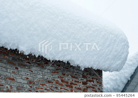There is a thick layer of snow on the roof of a brick building. A snowdrift on the roof. A snowy winter in Europe. The global problems of climate change. There is a thick layer of snow on the roof of a brick building. A snowdrift on the roof. A snowy winter in Europe. The global problems of climate change. 95445264