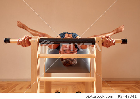 Handsome pilates male instructor performing stretching balance fitness exercise on small barrel equipment, at the pilates studio modern onterior indoor. 95445341