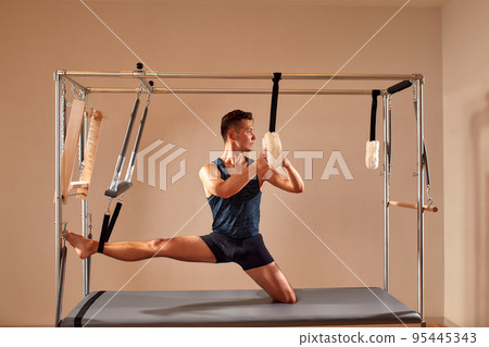 Side view of barefoot male athlete lying on pilates reformer and performing abs exercise during fitness workout. Pilates man concept. 95445343
