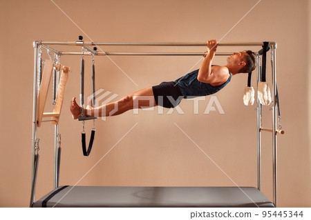 Fit man doing a lunge stretch yoga pilates exercise to strengthen and tone his muscles using a reformer in a gym 95445344
