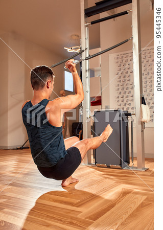 Side view of barefoot male athlete lying on pilates reformer and performing abs exercise during fitness workout. Pilates man concept. 95445346