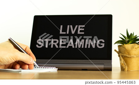 Live streaming symbol. Tablet with concept words Live streaming. Businessman hand with pen, house plant. Copy space. Beautiful white background. Business, live streaming concept, copy space. Live streaming symbol. Tablet with concept words Live streaming. Businessman hand with pen, house plant. Copy space. Beautiful white background. Business, live streaming concept, copy space. 95445863