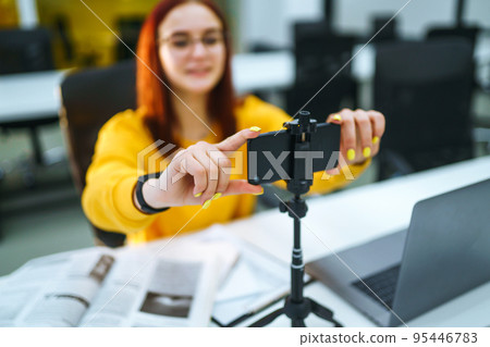 Hand woman holding camera for recording video. Teenager student in a yellow sweater with laptop. 95446783