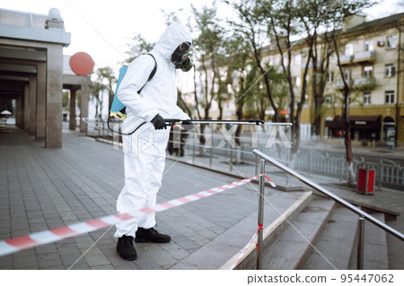 Man in protective suit and mask sprays disinfector onto the railing in the public place. Covid -19. Man in protective suit and mask sprays disinfector onto the railing in the public place. Covid -19. 95447062