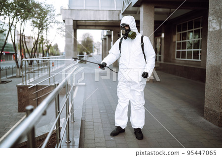 Man in protective suit and mask sprays disinfector onto the railing in the public place. Covid -19. Man in protective suit and mask sprays disinfector onto the railing in the public place. Covid -19. 95447065