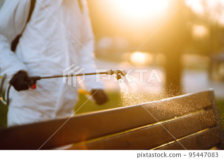 Man wearing protective suit disinfecting public places in the sun with spray chemicals. Covid -19. Man wearing protective suit disinfecting public places in the sun with spray chemicals. Covid -19. 95447083