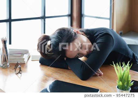 A portrait of a teenage Asian woman sleeping on a desk in the library due to fatigue from studying. A portrait of a teenage Asian woman sleeping on a desk in the library due to fatigue from studying. 95447275
